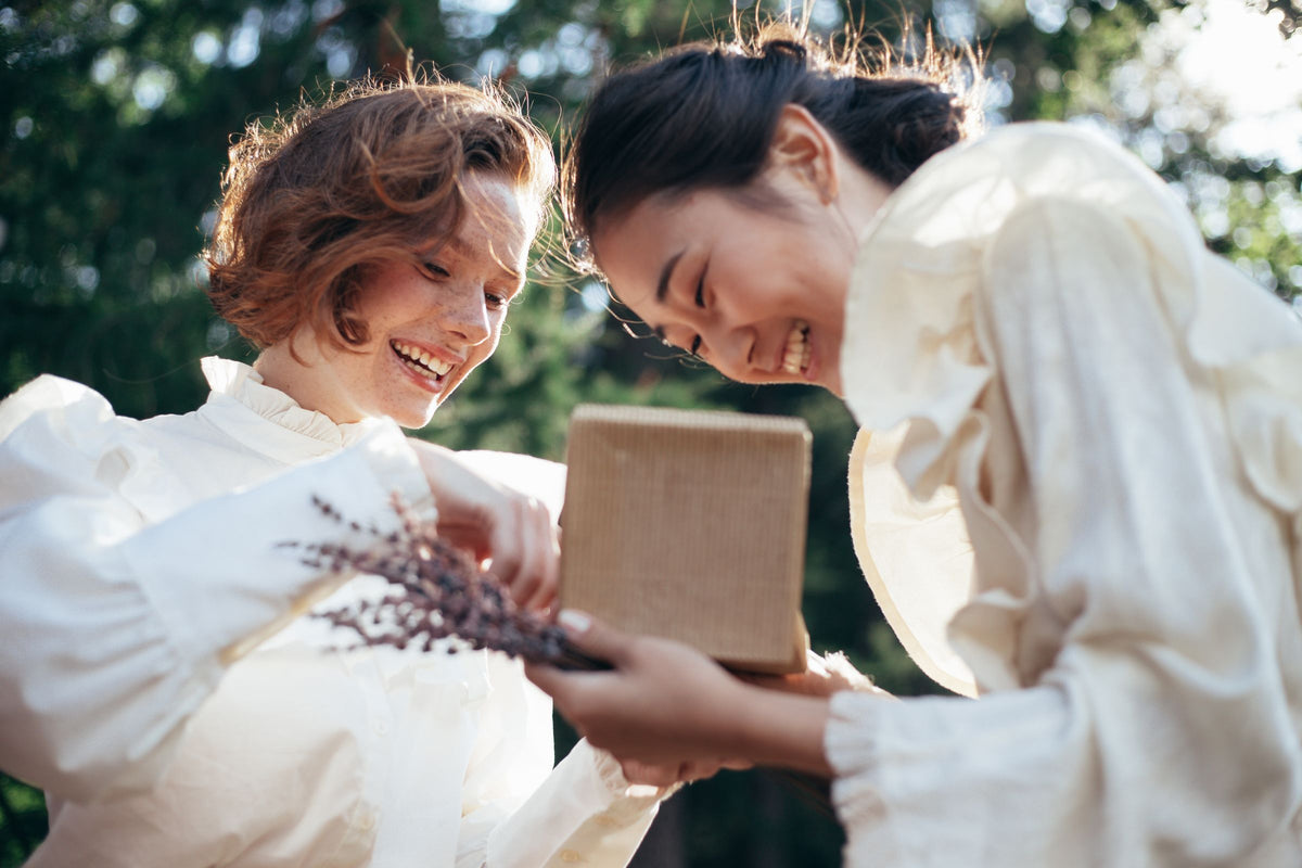 Two friends sharing a wrapped gift outdoors in soft natural light. Photo by Ron Lach.