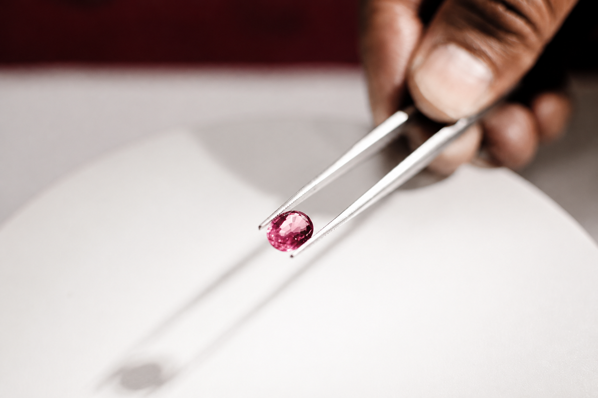 A pink faceted stone held in tweezers, an illustrative study of facets and light.