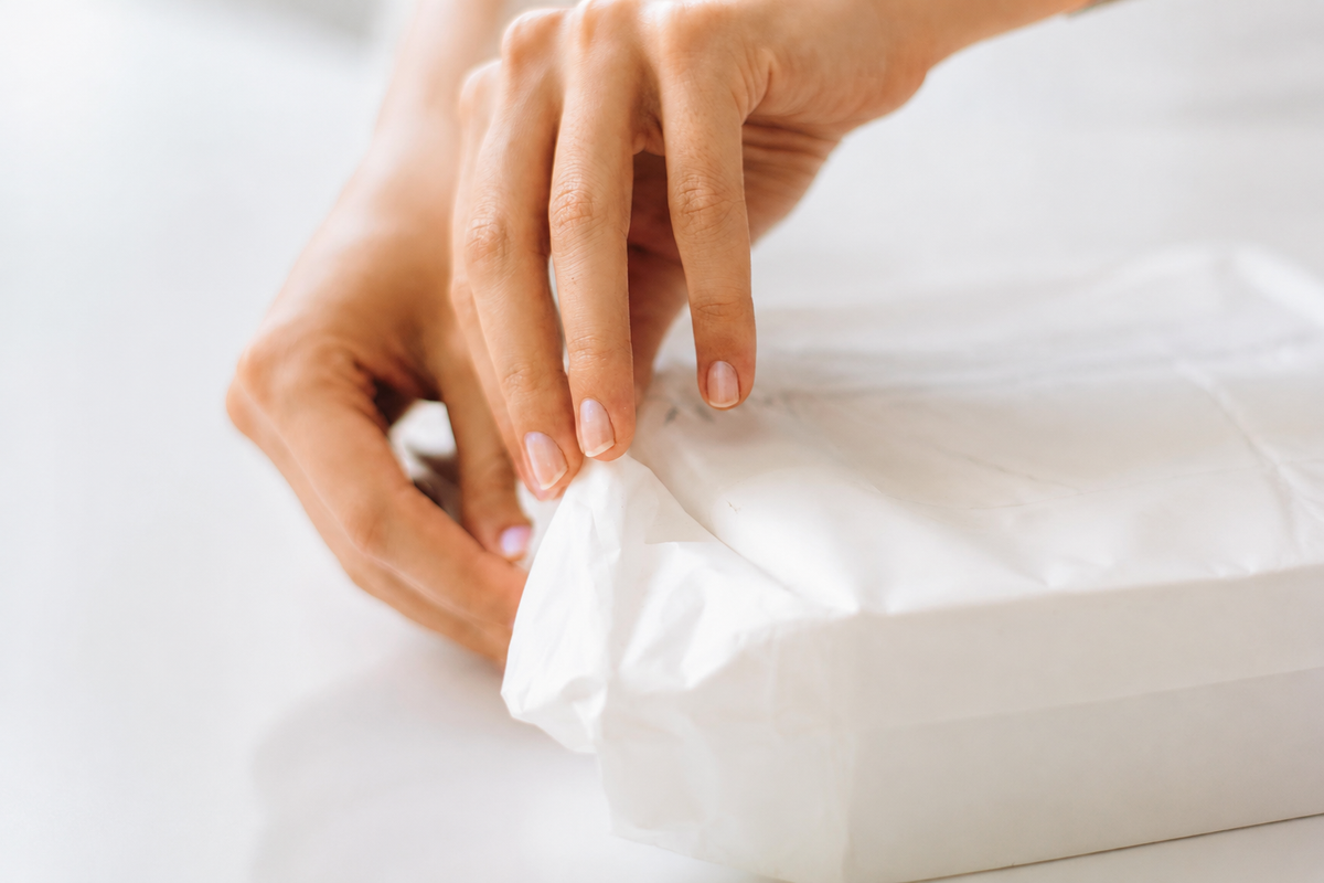 Hands folding white wrapping paper around a box; illustrative packaging photograph.