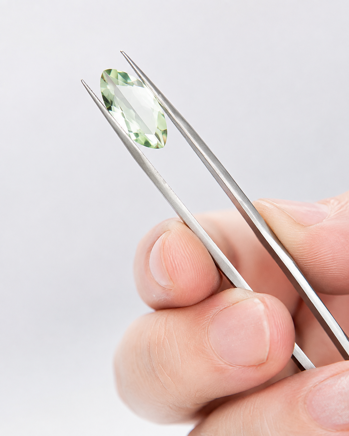 Pale green gemstone held in tweezers, an editorial study of facets and light