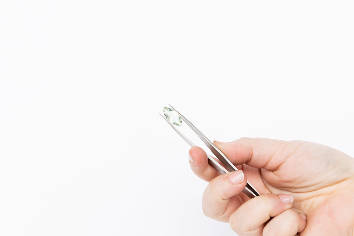 A pale green faceted stone held in tweezers, editorial material study.